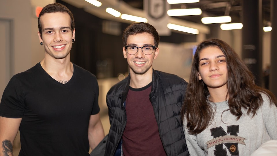 Deux jeunes hommes et une jeune femme sourient en regardant vers l'objectif.